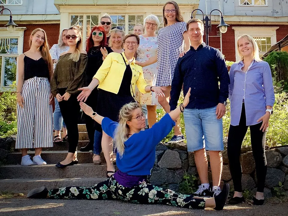 ProNeuronin työyhteisöä vanhan puutalon portailla kesäjuhlassa 2019. Etualalla yksi heistä tekee spagaatin.